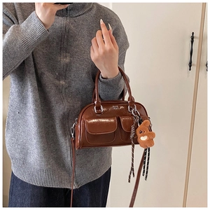 Détail du sac bowling en cuir verni marron avec poches frontales et breloque ours