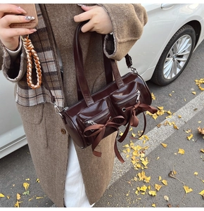 Détail d'un sac barillet en cuir verni marron foncé avec nœuds en soie et fermetures éclair
