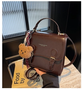 Detail of vintage coffee leather handbag with metal buckle and cute bear charm accessory