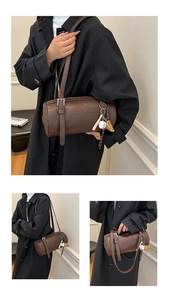 Macro shot of dark brown leather cylinder bag with embossed letters and baseball charm