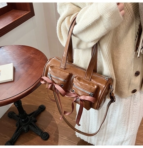 Détail d'un sac tonneau marron avec nœuds en satin rose et poches zippées frontales
