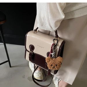 Detailed side view of vintage contrast-color handbag with teddy bear charm and strap