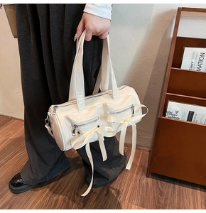 Détail d'un sac cylindrique blanc crème style ballet avec nœuds et fermetures éclair argentées