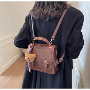Rear view of model wearing a vintage brown PU leather backpack with a plush bear charm
