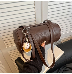 Detail of dark brown cylindrical leather bag with side embossing and baseball charm accessory