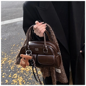 Détail du sac bowling brillant marron foncé avec poches avant et breloque ours en peluche