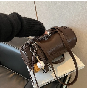 Detail of dark brown leather cylinder bag with embossed letters and a baseball charm