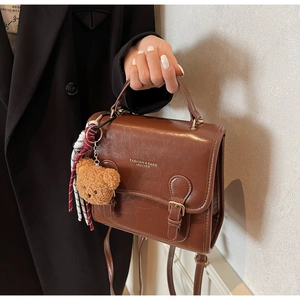 Detail showing brown vintage leather square bag with twin buckle straps and plush bear charm
