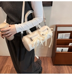 Détail d'un sac à bandoulière blanc cylindrique avec nœuds en soie et fermeture éclair