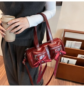 Détail du sac cylindre rouge foncé brillant avec nœuds porté par un modèle