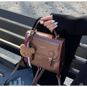 Detail of vintage brown leather handbag with metal buckles and cute plush bear charm