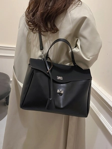 Minimalist black leather tote bag with silver metal twist locks shown on a model