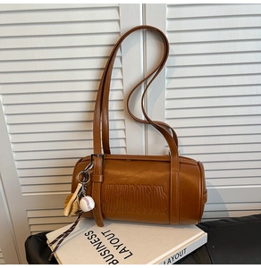 Close-up of brown leather cylinder bag with embossed letters and baseball charm detail