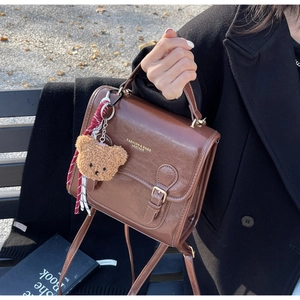 Detail of a vintage brown messenger bag with a plush bear charm and fashion leather print