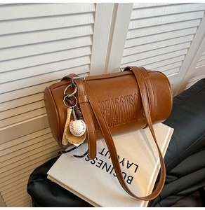 Macro detail of brown leather cylinder bag featuring embossed logo and sports charms