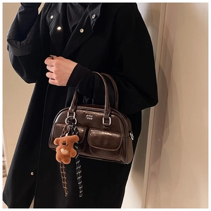 Détail d'un sac à main en cuir marron brillant avec deux poches avant et un porte-clé ours