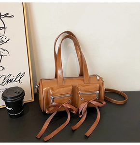 Détail d'un sac baril marron brillant avec des nœuds en ruban et deux poches zippées