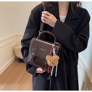 Detail of vintage dark brown square handbag with crackle texture and bear charm