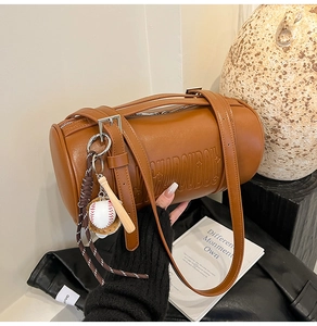 Detailed close-up of brown leather cylinder bag featuring embossed logo and baseball charms