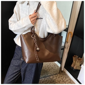 Detail of a dark brown tote bag with decorative silver bell and knotted strap on shoulder