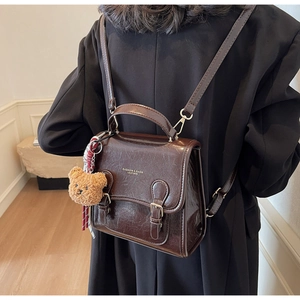 Detail view of retro brown faux leather backpack with plush bear charm and buckle straps