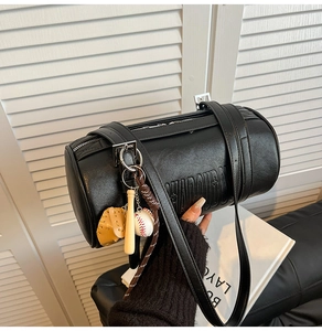 Detail of black cylindrical barrel bag featuring sports-themed charms and letter embossing