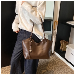 Close-up of a large brown leather tote bag featuring a metal ring and woven pendant detail
