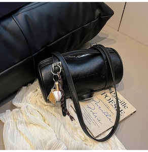 Detail of black cylinder pillow bag with embossed letters and a baseball-themed charm