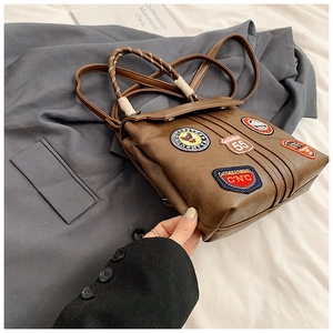 Detail of vintage brown PU leather backpack with retro embroidery patches and woven handle