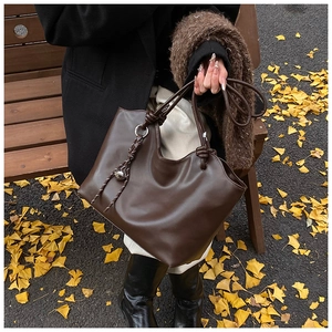 Detail of knot handle and braided silver ring charm on dark brown leather tote bag
