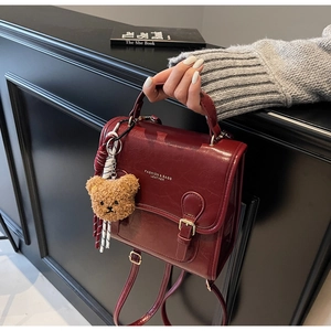 Macro shot of burgundy vintage crossbody bag with a metal buckle and a cute bear charm