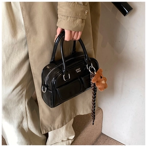 Détail d'un sac bowling en cuir verni noir avec poches avant et un charmant ours peluche