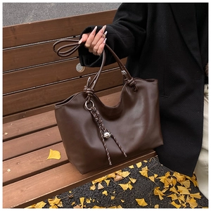 Detail of dark brown matte PU leather tote bag with knotted strap on an autumn bench