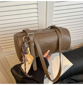 Close-up of brown leather cylinder bag with baseball charm and embossed letters