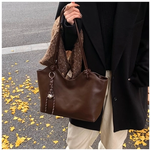 Brown leather tote bag featuring a decorative metal bell charm and knot strap details