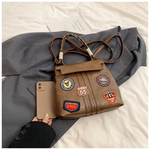 Detail of vintage brown leather handbag with American style embroidery patches and woven handle