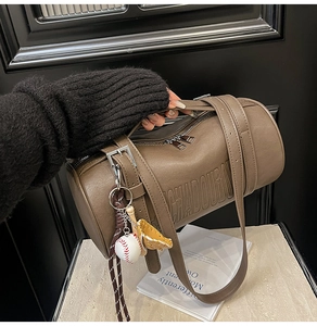 Detail view of brown barrel bag featuring embossed lettering and a baseball charm
