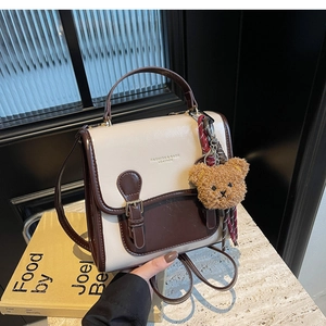 Detail of retro color-block handbag with metal buckle and plush bear pendant accessory