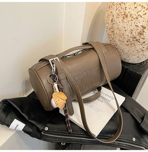 Detail of brown matte cylinder bag with embossed letters and unique baseball glove charm
