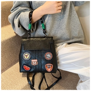 Close-up of black leather backpack featuring vintage patches and a rope handle detail