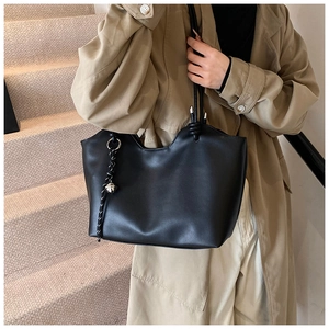 Detail of minimalist black leather tote bag with unique wave edge and knot strap on model