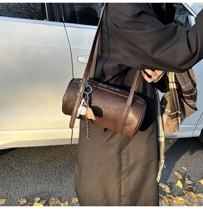 Detail of dark brown cylindrical crossbody bag with DUUDOU embossed texture and baseball charm