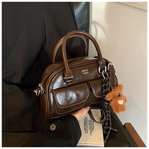 Détail d'un sac bowling marron foncé en cuir ciré avec charme d'ours et sangle