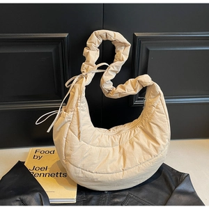 Detail of beige quilted dumpling bag with ruched shoulder strap and drawstring accents