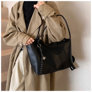 Detail of a large black faux leather tote bag with braided charm on a stylish model