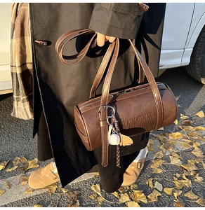 Detail of vintage brown leather cylinder bag with embossed texture and baseball charm