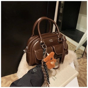 Détail d'un sac bowling marron foncé brillant avec poches avant et breloque petit ours