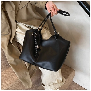 Detail of a black leather tote bag featuring braided knot charms and a wavy rim edge