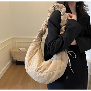 Detail of ruched shoulder strap and beige half-moon dumpling bag on model crossbody