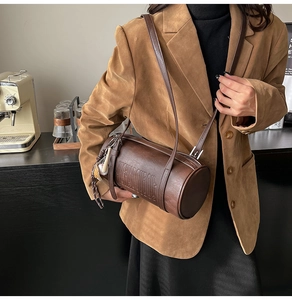 Close-up of brown leather cylinder bag featuring vintage texture and embossed logo detail